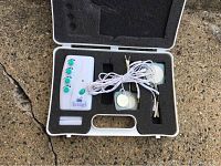 Opened case showing IGIA ElectroSage 8 control unit with four green dial knobs and connected electrode pads with white wires in foam insert.