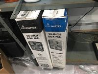 Two boxed Coolmaster 20-inch box fans on shelf.