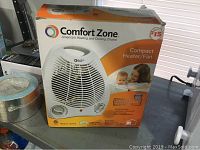 Photo of the original box packaging for the Comfort Zone compact heater fan with branding and product image visible.