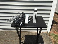 Wii console with controllers and cables on a small black table outdoors