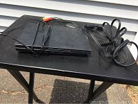 PlayStation 2 Slim console with power cable and AV cable placed on a black table outside.