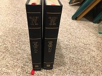 Two black hardcover books standing upright on carpet, showing spine titles with gold text including series title, volume number, and author.