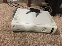 View of white Xbox 360 console with hard drive and WiFi antenna on top, placed on carpeted floor