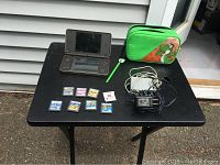 Full lot setup including Nintendo DSi XL, game cartridges, chargers, and Yoshi case displayed on black table outside.