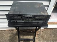 Full frontal view of Crown Ultra-Tech 1010 amplifier, showing front panel, brand logo, and vent grille, set on a black folding table outdoors.