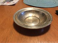 Top angled view of round sterling silver bowl showing decorative rim and dented area in center.