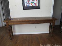 Sofa table shown from front angle, placed against a wall with a painting above it. Table shows visible surface wear including chips and scratches on the wood top and legs.