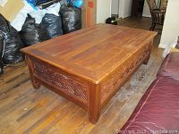 Top-front angle view of large rectangular teak wood coffee table showing carved wooden side panels and visible wear on the surface