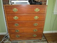 Front view of teak dresser showing five drawers and brass-colored handles. Visible wear and chips on wood finish.
