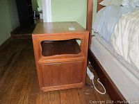 Pair of teak nightstands positioned on hardwood floor, one shown from the side near bed.
