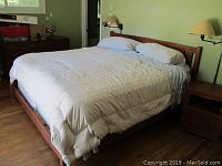 Full view of king size bed with cherry wood frame, headboard, mattress, white comforter and pillows.