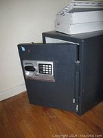 Black Sentry safe with door open revealing white interior with soiling and uninstalled locking bars/drawers beside it.
