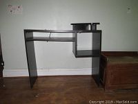 Front view of the dark brown MDF desk against a light colored wall with visible chips on edges.