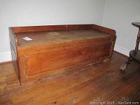 Front angled view of teak wood storage chest with lid closed on hardwood floor.