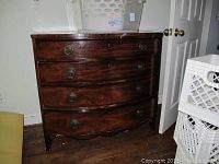 Front view of a dark wood dresser with four drawers and brass-colored hardware showing wear, chips, and scratches.