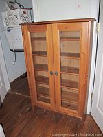 Front view of wooden media cabinet with two glass doors and metal handles standing on wooden floor.