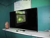 Front view of Samsung 32 inch flat screen TV on shelf with remote.