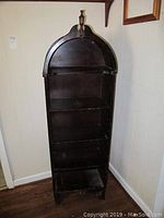 Front view of dark wooden bookcase with arched top and decorative finial at top center. Four stationary shelves inside. Visible chips and scratches on wood surface.