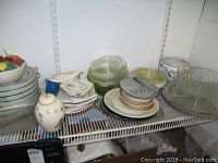 Photo of assorted dishes on wire rack including ceramic vase, glass and ceramic mixing bowls, covered fruit motif serving bowls, plates, and butter dishes.