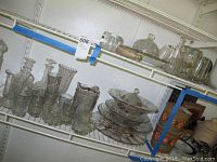 Wide view of shelves holding the glassware items including pitchers, glasses, serving platters, and bowls.