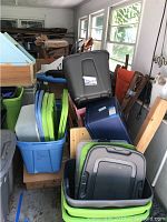 View showing stacked plastic storage bins in blue, green, gray, and black colors with lids, wooden items and parts of furniture visible at the back.