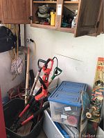 Overview of yard tools including Black & Decker hedge trimmer, shovels, spade, branch clippers, plastic bins, skateboard and kite leaning nearby