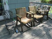 Full view showing three wooden slatted deck chairs, two bare and one with cushions, plus the metal garden chair with floral pattern on back and legs.