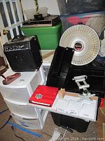 Wide angle photo showing plastic storage cubby with three drawers, black amplifier, red office folder, white Presto Heat Dish, and mounting hardware.
