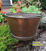 Side view of the large round copper pot showing hammered copper surface and handle attachment with rivets.