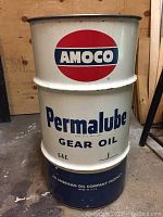 Full view of Amoco 25 gallon oil drum with Permalube Gear Oil branding, clean exterior, set on concrete floor against wood wall.