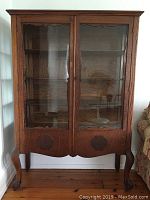 Front view of large oak china cabinet with glass front doors, showing wood grain, glass panels and claw feet on front legs