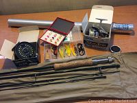 Photo showing the 9-foot multi-piece Cortland fly fishing rod with cork handle, fly reel, spinning reel, aluminum carrying case, and two fly boxes with various fishing flies.