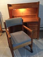 Solid wood desk with attached hutch, work light illuminated, showing the structure and drawers; upholstered chair positioned in front