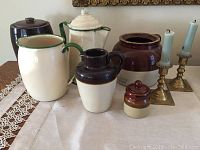 Image showing a group of stoneware crocks and pitchers alongside two brass candlesticks, all arranged on a cloth.