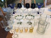 Photo showing a variety of blue, black, clear, and painted glasses including margarita and martini glasses, with beer mugs and shot glasses at front.