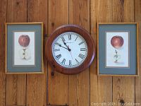 Wall clock flanked by two framed apple prints hung on wood panel wall