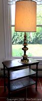 Woodend table with brass-colored lamp on top near a window showing the end table surface, shelves, and lamp details
