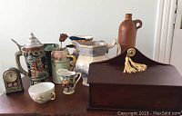 Lot of assorted ceramic and decorative items including pitchers, stein, vase, bottle, candle box, clock, and bowl arranged on a table.
