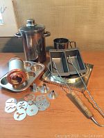 Photo showing baking and cooking tools arranged including cookie press, metal baking trays, tongs, flour sifter, measuring cup, and asparagus steamer