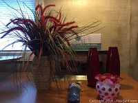 View of two tall, thin red vases, beige textured vase with red, green, and yellow dried flowers, blue ceramic wall hanging vase, ladybug ceramic vase, and Martha Stewart cake stand box.