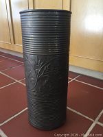 Full view of brass tinted stamped metal umbrella stand showing ribbed top and bottom bands and floral design in middle