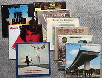 Lot overview of 9 vinyl LP record album covers laid flat on carpet. Visible albums include The Band - Islands, The Doors Greatest Hits, Rolling Stones live concert, Woodstock 3-record set, Cat Stevens - Tea for the Tillerman, and others.