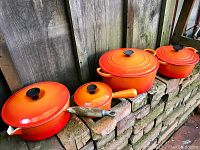 All four pieces—sauté pan with wooden handle, small saucepan, medium and large Dutch ovens—arranged on brick ledge
