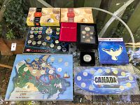 Overview of eight sealed coin sets and medallions on glass table