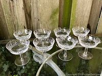 Eight Waterford crystal stemware glasses arranged in two rows on a glass table, showing the diamond-cut Alana pattern clearly from different angles.