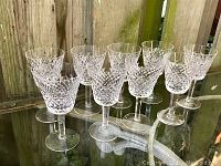 Nine Waterford Crystal stemware glasses arranged on a glass table with a wooden fence background, showing the diamond-cut Alana pattern.