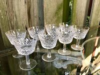 Eight Waterford Crystal Alana parfait glasses on a clear surface with a wooden fence background, showing intricate cut crystal pattern and overall shape.