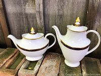 Both teapot and coffee pot side by side on brick surface with wooden fence background