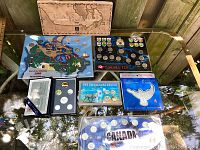 Image showing all coin sets displayed together on a glass table in their sealed packaging with various designs including maps and wildlife.