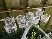 Eight crystal napkin rings arranged on reflective glass table with wooden fence background